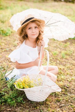 Işık ile tatlı bir küçük kız bir hasır şapka, beyaz bir elbise ve dantel şemsiye yaz tarlada çiçekler bir sepet ile bukleler. Yaz aylarında kırsal yaşam