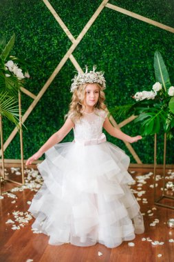 Beyaz gelinlik ve çelenk çiçek süslemeleri yapılmış tropik yapraklar, beyaz güller ve orkide çiçek dolu sarışın kıvırcık saçlı sevimli küçük kız