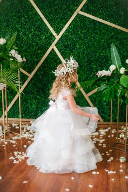 Beyaz gelinlik ve çelenk çiçek süslemeleri yapılmış tropik yapraklar, beyaz güller ve orkide çiçek dolu sarışın kıvırcık saçlı sevimli küçük kız