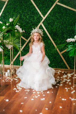 Beyaz gelinlik ve çelenk çiçek süslemeleri yapılmış tropik yapraklar, beyaz güller ve orkide çiçek dolu sarışın kıvırcık saçlı sevimli küçük kız