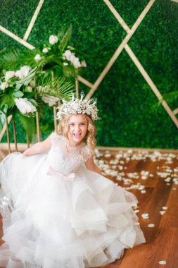 Beyaz gelinlik ve çelenk çiçek süslemeleri yapılmış tropik yapraklar, beyaz güller ve orkide çiçek dolu sarışın kıvırcık saçlı sevimli küçük kız