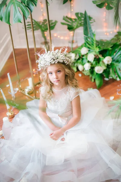 Beyaz gelinlik ve çelenk çiçek süslemeleri yapılmış tropik yapraklar, beyaz güller ve orkide çiçek dolu sarışın kıvırcık saçlı sevimli küçük kız