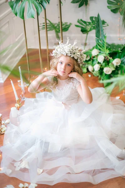 Beyaz gelinlik ve çelenk çiçek süslemeleri yapılmış tropik yapraklar, beyaz güller ve orkide çiçek dolu sarışın kıvırcık saçlı sevimli küçük kız