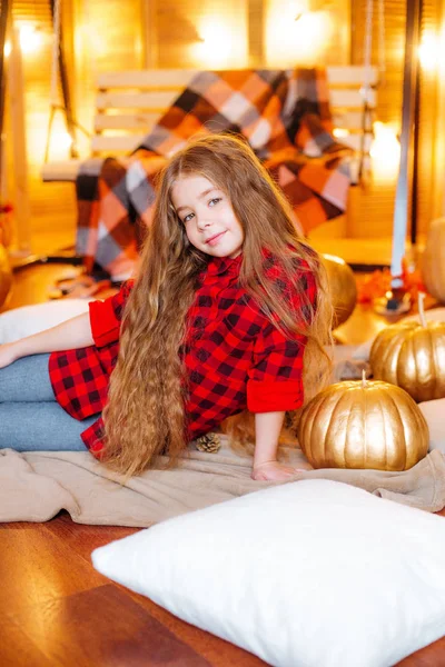 小可爱的女孩与长卷曲的头发附近的秋千和南瓜在红色方格衬衫和毯子 — 图库照片