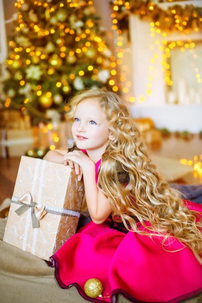 かわいい装飾が施された暖炉と花輪ギフト クリスマス ツリー近く自宅のブロンド髪長い巻き毛の女の子 — ストック写真