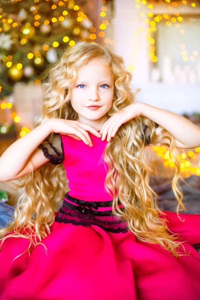 可爱的小女孩与长卷发金发在家里附近的圣诞树与礼品和花环和装饰的壁炉 — 图库照片