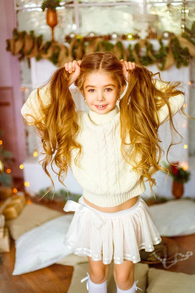 可爱的小女孩与金发长卷发在一个光针织毛衣由节日壁炉与花环和蜡烛 — 图库照片