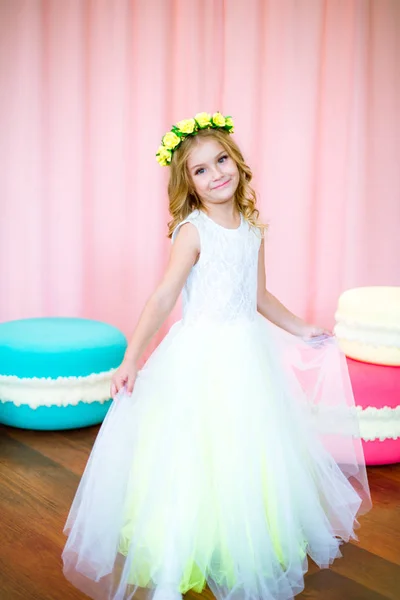 ピンクの背景のスタジオで巨大なお菓子と白い緑豊かなドレスを着たブロンドのカールとかわいい女の子 — ストック写真