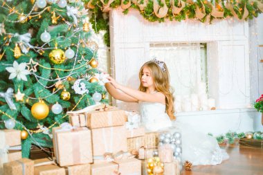 Uzun kıvırcık saçlı evde hediyeler ve çelenk ve dekore edilmiş bir şömine ile Noel ağacı yakınındaki sevimli küçük kız 