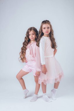 Sevimli küçük kız beyaz moda giysiler içinde kıvırcık saçlı ve pembe stüdyo