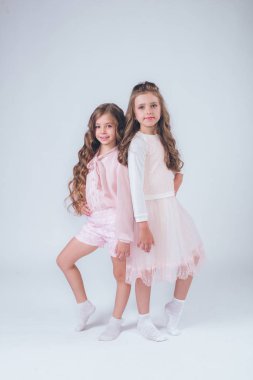 Sevimli küçük kız beyaz moda giysiler içinde kıvırcık saçlı ve pembe stüdyo