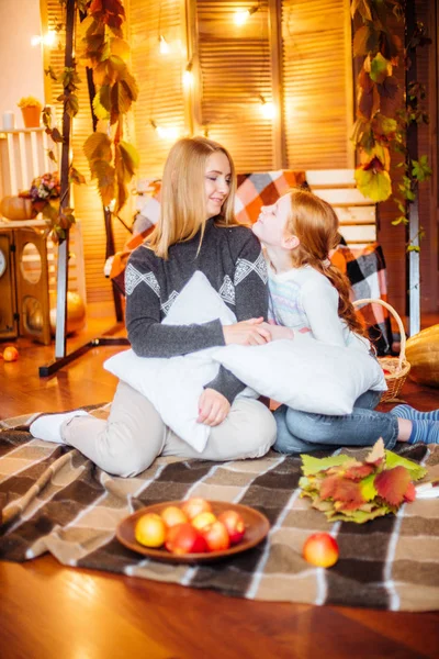 Red-haired teen girl and her mom in the studio in the fall scenery with yellow leaves, blankets, apples and pumpkins