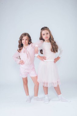 Sevimli küçük kız beyaz moda giysiler içinde kıvırcık saçlı ve pembe stüdyo