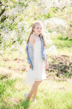 Yemyeşil bir bahçede bahar beyaz bir sundress sarışın saçlı sevimli kız