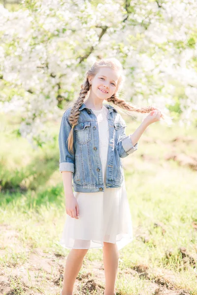 可爱的女孩与金发在白色的太阳礼服在春天在郁郁葱葱的花园 — 图库照片