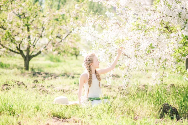 水仙の花と緑豊かな庭園で春に白いサンドレスで金髪のかわいい女の子 — ストック写真