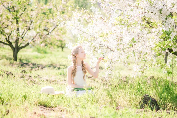 水仙の花と緑豊かな庭園で春に白いサンドレスで金髪のかわいい女の子 — ストック写真