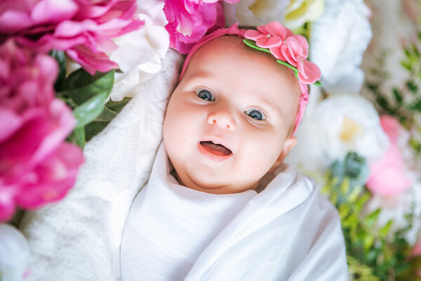 Newborn baby in a flower dressing lies in spring flowers
