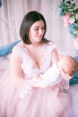 Bir kadının küçük özel odası elbiseli genç anne bahar çiçekleri gölgelik yatak tarafından kucağında bir bebekle