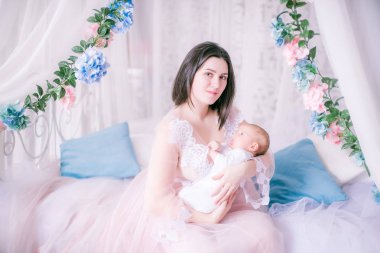 Bir kadının küçük özel odası elbiseli genç anne bahar çiçekleri gölgelik yatak tarafından kucağında bir bebekle