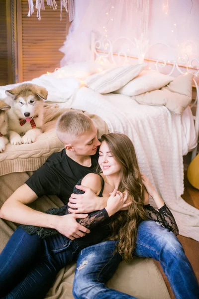 マラミュートの子犬との愛を表現しながら寝室に座ってうれしそうな若い夫婦 — ストック写真