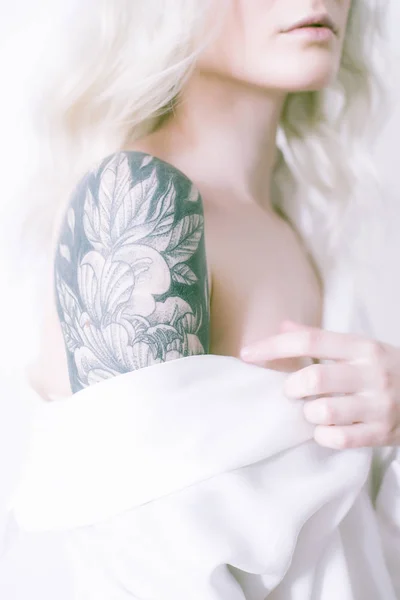 Attractive girl with blond hair and a tattoo on her arm in a white shirt