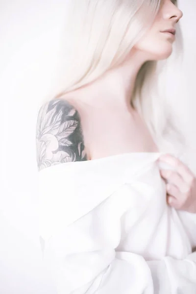 Attractive girl with blond hair and a tattoo on her arm in a white shirt