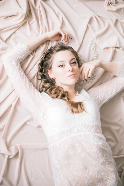 Young cute bride with beautiful hairdo morning at home in white lace negligee