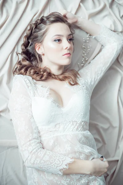 Young cute bride with beautiful hairdo morning at home in white lace negligee