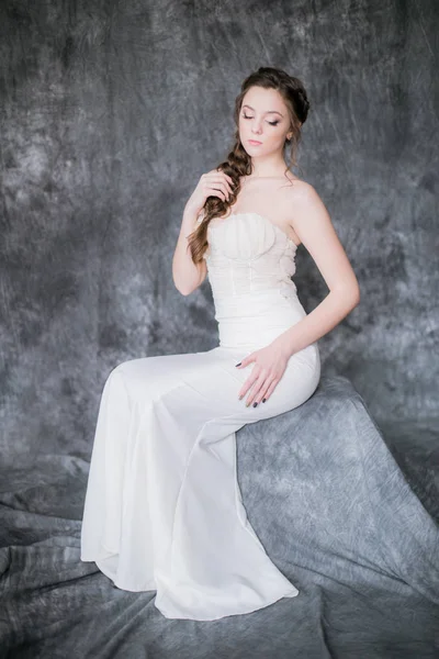 Young cute bride with beautiful hairdo in a white dress on a gray background in the studio