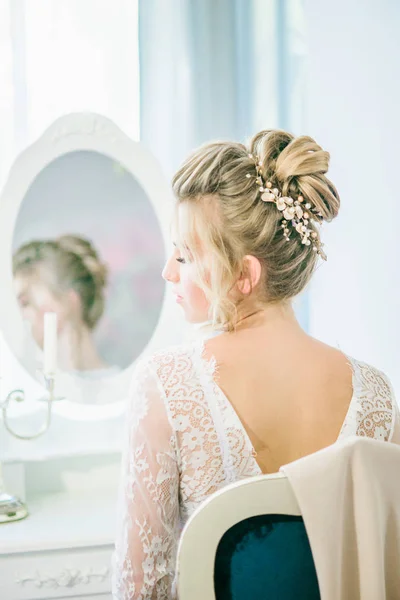 Young cute bride with a beautiful hairdo in the morning at home at the dressing table in white lace negligee