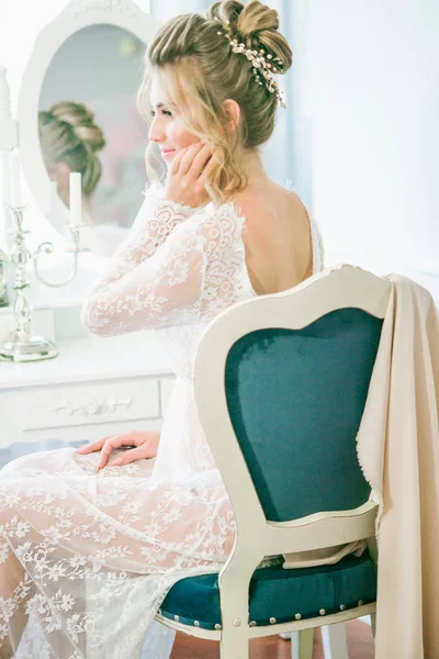 Young cute bride with a beautiful hairdo in the morning at home at the dressing table in white lace negligee