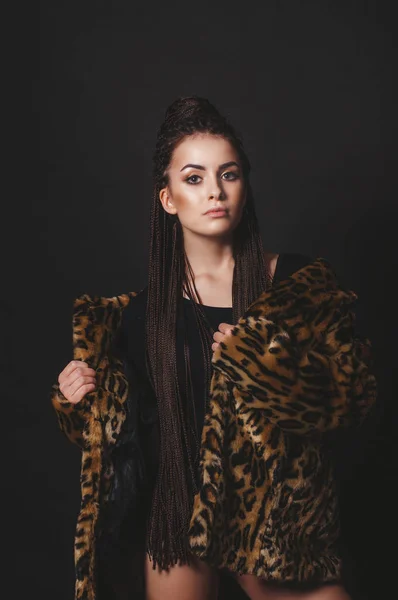 黒の背景の上のヒョウの毛皮の下で毛皮のコートの長いアフロ三つ編みを持つ魅力的な少女 — ストック写真