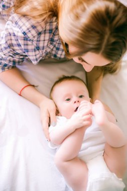 Gömlek ve mavi jeans erkek bebek onun yatak - görüntü ile oynarken güzel anne portresi