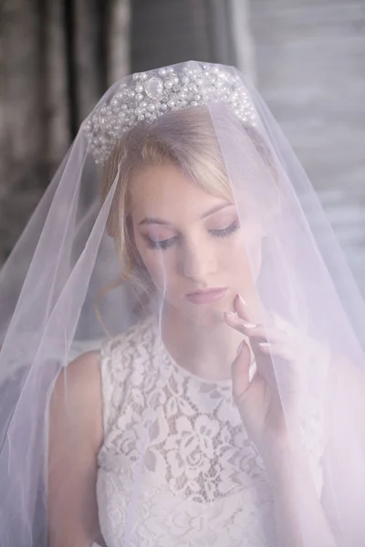 Young beautiful bride with blond hair in a diadem and white veil and white dress