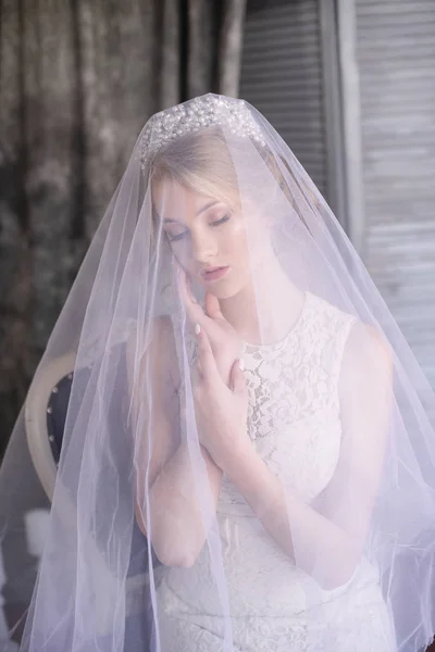 Young beautiful bride with blond hair in a diadem and white veil and white dress