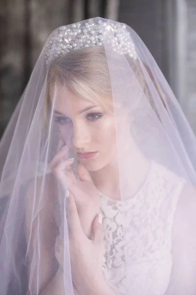 Young beautiful bride with blond hair in a diadem and white veil and white dress