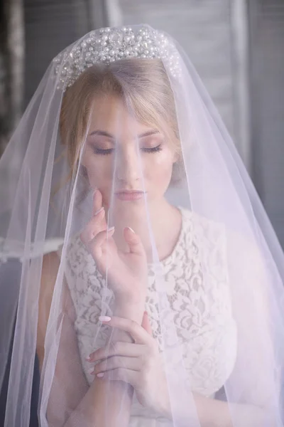 Young beautiful bride with blond hair in a diadem and white veil and white dress