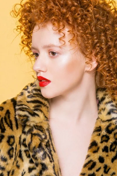 年轻明亮的模型与红色卷曲的头发和豹子趋向外套在黄色背景 — 图库照片