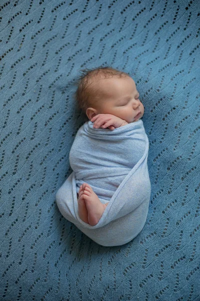 Cute little baby in blue blanket is sleeping on the bed at home