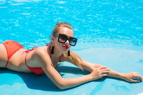 时尚户外照片美丽的女孩与金发穿着豪华的红色泳衣 摆姿势在游泳池旁边 — 图库照片