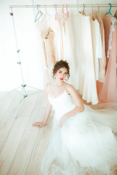 Beautiful young bride in a white dress in the salon on the background of other wedding dresses