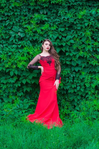 緑の夏の庭の通りに唇に赤い口紅と夜のファッショナブルな赤いドレスで長い髪を持つ美しい若い女の子 — ストック写真