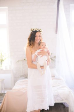 Beyaz bir elbiseyle kiraz çiçekleri içinde genç, tatlı bir anne bahar yatak odasında kollarında çiçek açan kiraz dallarıyla bir bebek tutuyor.