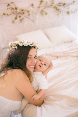 Beyaz bir elbiseyle kiraz çiçekleri içinde genç, tatlı bir anne bahar yatak odasında kollarında çiçek açan kiraz dallarıyla bir bebek tutuyor.