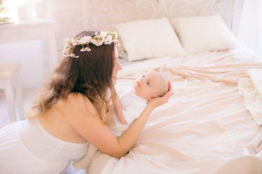 Beyaz bir elbiseyle kiraz çiçekleri içinde genç, tatlı bir anne bahar yatak odasında kollarında çiçek açan kiraz dallarıyla bir bebek tutuyor.