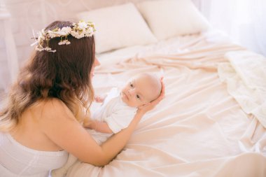 Beyaz bir elbiseyle kiraz çiçekleri içinde genç, tatlı bir anne bahar yatak odasında kollarında çiçek açan kiraz dallarıyla bir bebek tutuyor.