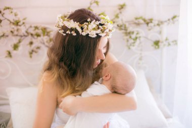 Beyaz bir elbiseyle kiraz çiçekleri içinde genç, tatlı bir anne bahar yatak odasında kollarında çiçek açan kiraz dallarıyla bir bebek tutuyor.