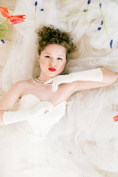 年轻美丽的新娘穿着80年代风格的白色婚纱 嘴唇上涂着红色口红 用郁金香涂在地板上 — 图库照片