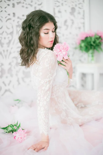 美丽的年轻女孩在一个明亮的工作室与牡丹花的白色蕾丝连衣裙 — 图库照片